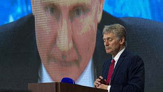 Dmitrij Peszkov, a Kreml szóvivője Putyin orosz elnökkel a háttérben, aki online jelentkezett be egy sajtótájékoztatóra 2020 decemberében.