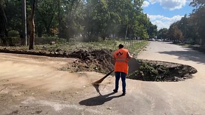 Woman sweeps street next to huge crater created from shelling