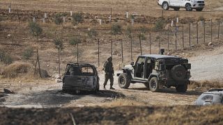 جندي إسرائيلي بالقرب من سيارة محترقة استخدمها فلسطينيون خلال هجوم إطلاق نار على حافلة إسرائيلية في غور الأردن بالضفة الغربية. 2022/09/04
