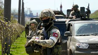 Russian servicemen stand near their military vehicles in Berdiansk with the Azov Sea in the background,