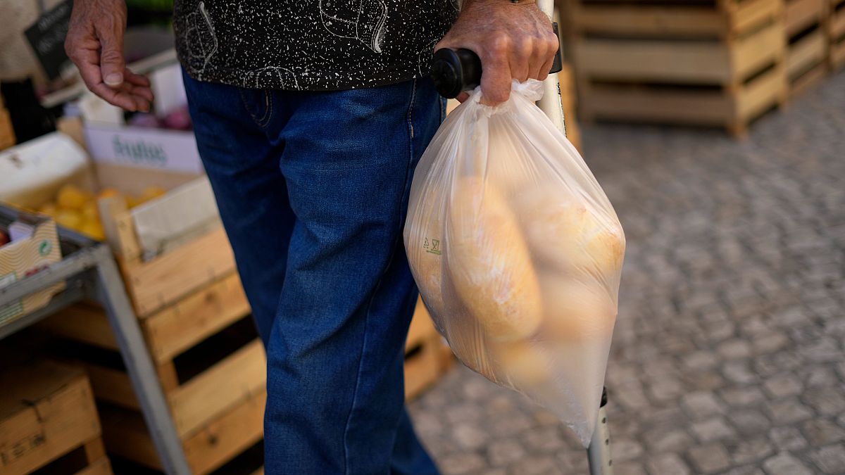 رجل يحمل كيسا به خبز يمشي أمام محل بقالة في لشبونة. 2022/09/05