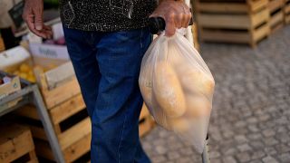 رجل يحمل كيسا به خبز يمشي أمام محل بقالة في لشبونة. 2022/09/05