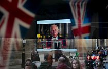 A passer-by tries to catch a glimpse of the televised speech of the new King Charles III as she passes by a pub in London, Friday, Sept. 9, 2022. 