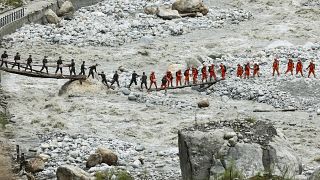 Ideiglenesen felállított hídon adogatják át egymásnak a földrengés rászorulóinak szánt ellátmányt egy kínai mentőalakulat tagjai 2022. szeptember 8-án.