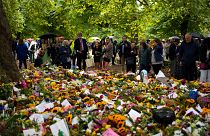 People gather in front of flowers for late Queen Elizabeth II at Green Park, near Buckingham Palace in London, Tuesday, Sept. 13, 2022.