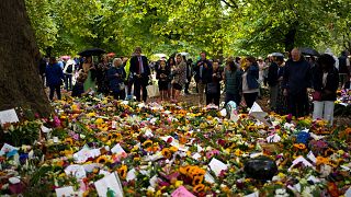 People gather in front of flowers for late Queen Elizabeth II at Green Park, near Buckingham Palace in London, Tuesday, Sept. 13, 2022.