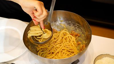 A woman spoons onto a plate some "spaghetti alla Carbonara" during a cooking competition on the eve of the Carbonara Day