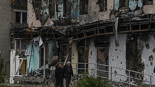Casal em frente a edifício destruído em Izyum
