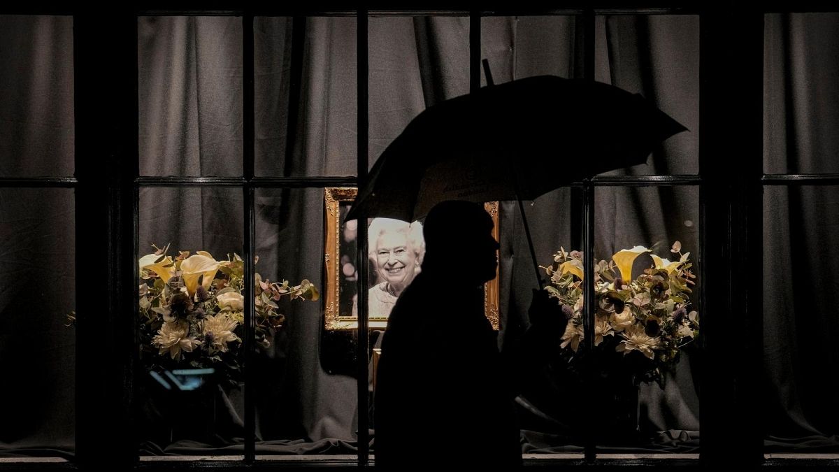A man walks by a portrait of Queen Elizabeth II during a rainfall in central London, Tuesday, Sept. 13, 2022