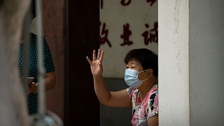 A woman wearing a face mask waves to a person at a public park in Beijing, Tuesday, Sept. 13, 2022. 