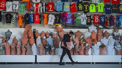 A shop clerk carries mannequins at a soccer jerseys stand at a tourist shopping area, in Belek, 12 March 2022