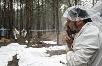 Expert smokes under the rain during the exhumation of bodies in the recently retaken area of Izium, 16 September 2022
