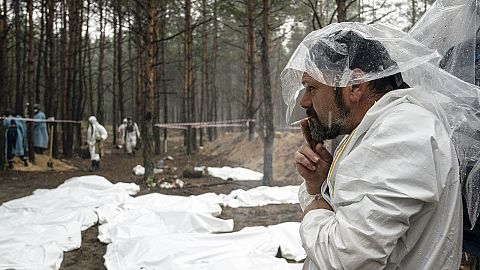 Expert smokes under the rain during the exhumation of bodies in the recently retaken area of Izium, 16 September 2022