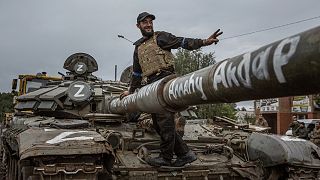 A Ukrainian soldier near the entrance of Izium does a peace sign standing on a captured Russian T tank.