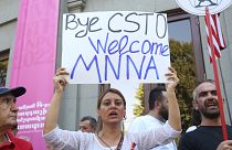 A woman holds a poster reading ''Bye Collective Security Treaty Organization welcome Major non-NATO ally'' as other demonstrators gather in Yerevan.