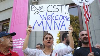 A woman holds a poster reading ''Bye Collective Security Treaty Organization welcome Major non-NATO ally'' as other demonstrators gather in Yerevan.