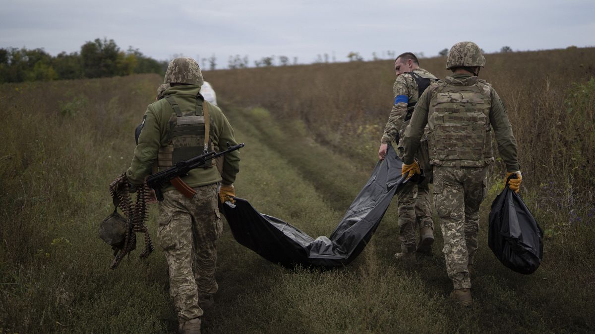 Ukrainian servicemen carry a bag containing the body of a Ukrainian soldier, centre, and a Russian soldier's remains, right. Saturday, 17 September 2022.