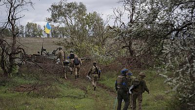 Ukrainian national guard servicemen walk next to a damaged Russian tank