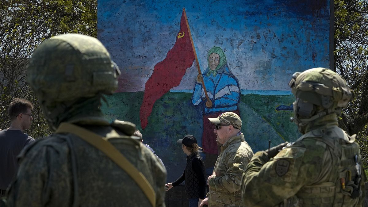 ussian servicemen stand near a painting of a woman holding a Soviet-era red flag in territory under the government of the so-called Donetsk People's Republic, in April 2022