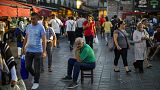 A man sits as people walk past by at the Egyptian spices market in Istanbul, Turkey, Thursday, Aug. 18, 2022.