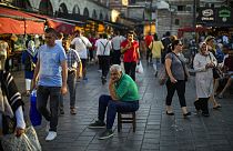 A man sits as people walk past by at the Egyptian spices market in Istanbul, Turkey, Thursday, Aug. 18, 2022.