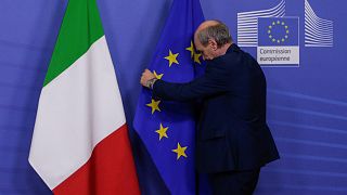 Employee fixes flags before the European Commission President receives the Italian Prime Minister for a meeting on December 12, 2018, in Brussels. 