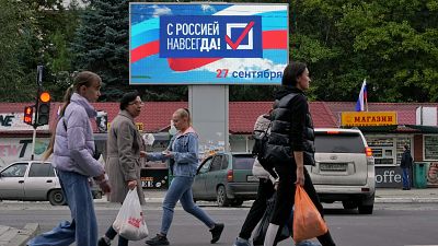 People walk past a billboard reading 'Forever with Russia' in Luhansk, eastern Ukraine, Tuesday, Sept. 27, 2022