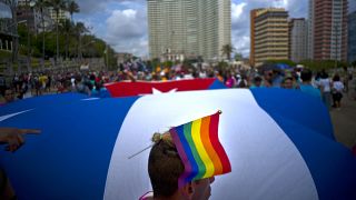 Un hombre lleva una bandera de mano del arco iris en la cabeza con la bandera nacional de Cuba como telón de fondo durante una marcha del orgullo