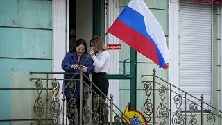Zwei Frauen in  Luhansk befestigen eine russische Flagge an einem Treppengeländer
