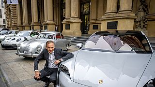 Le PDG du constructeur automobile Porsche, Oliver Blume, s'agenouille à côté de voitures Porsche au début de la cotation de Porsche à la bourse de Francfort