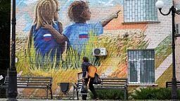 A man walks past a graffiti depicting children with Russian flags in Luhansk