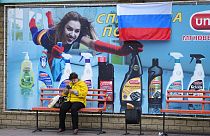 A woman waits at a bus stop with an advertising poster, a day after voting in four Moscow-held regions of Ukraine on referendums to become part of Russia.