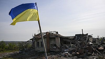 Eine ukrainische Fahne weht vor einem zerstörten Gebäude