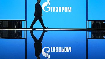 A man walks at an exhibition at the St. Petersburg International Gas Forum in St. Petersburg, Russia, Wednesday, Sept. 14, 2022, with a logo of Russian gas monopoly Gazprom in