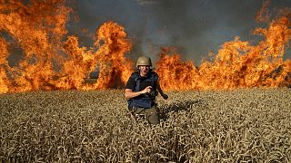 A journalist runs from a burning wheat field during his assignment after Russian shelling, a few kilometres from Ukrainian-Russian border in the Kharkiv region, July 29, 2022.