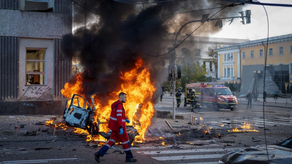 A medical worker runs past a burning car after a Russian attack in Kyiv, Ukraine, Monday, Oct. 10, 2022.