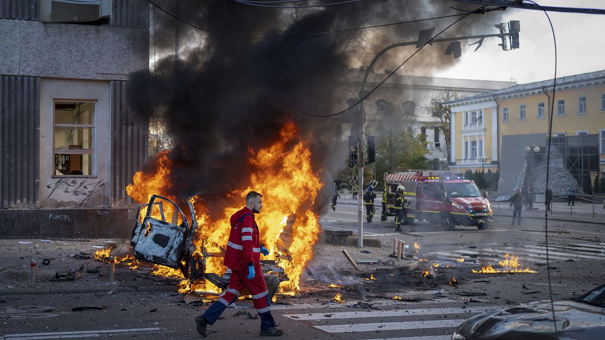 Un travailleur médical marche à côté d'une voiture qui brûle suite aux attaques à Kyiv, le 10 octobre 2022.