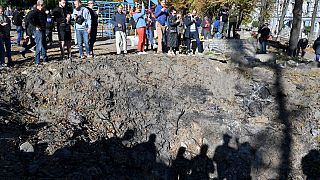 People stand by a rocket crater next to a child playground in central Kyiv on October 10, 2022 after Ukraine's capital was hit by multiple Russian strikes.