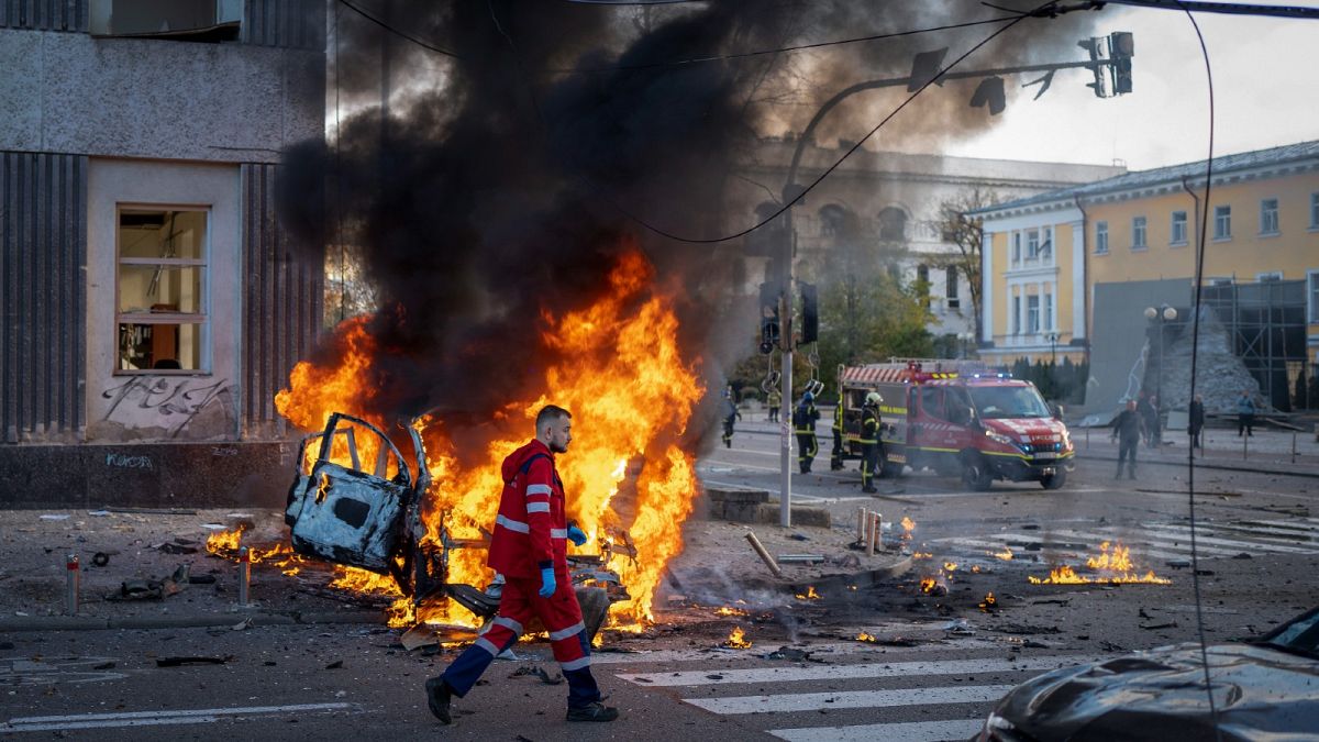 A medical worker runs past a burning car after a Russian attack in Kyiv, Ukraine, Oct. 10, 2022.