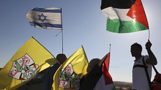 فلسطينيون يرفعون علمهم الوطني وعلم فتح وهم يقفون بالقرب من جنود إسرائيليين يؤمنون مسيرة للمستوطنين الإسرائيليين، بالقرب من الخليل بالضفة الغربية المحتلة، في 21 يونيو 2021