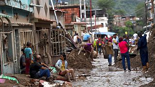 Residentes locales descansan mientras sus vecinos limpian el barro y recuperan sus pertenencias en una calle inundada mientras el sol se pone en Las Tejerías, Venezuela