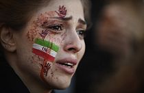 A demonstrator with an Iranian flag and red hands painted on her face attends a rally in support of Iranian protests, in Paris on October 9, 2022.