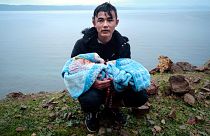A migrant holding a baby pauses on the side of the road on the Greek island of Lesbos, after crossing on a dinghy the Aegean Sea from Turkey.