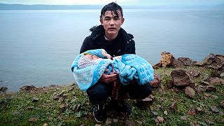 A migrant holding a baby pauses on the side of the road on the Greek island of Lesbos, after crossing on a dinghy the Aegean Sea from Turkey.