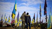 ARQUIVO - Pais de um militar ucraniano recentemente morto estão ao lado do seu túmulo, 14 de outubro de 2022.
