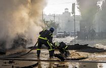 A firefighter helps his colleague to escape from a crater as they extinguish smoke from a burned car after a Russian attack in Kyiv, Ukraine, Monday, Oct. 10, 2022.