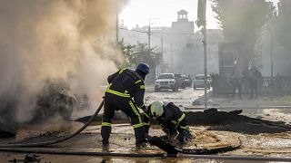 A firefighter helps his colleague to escape from a crater as they extinguish smoke from a burned car after a Russian attack in Kyiv, Ukraine, Monday, Oct. 10, 2022. 