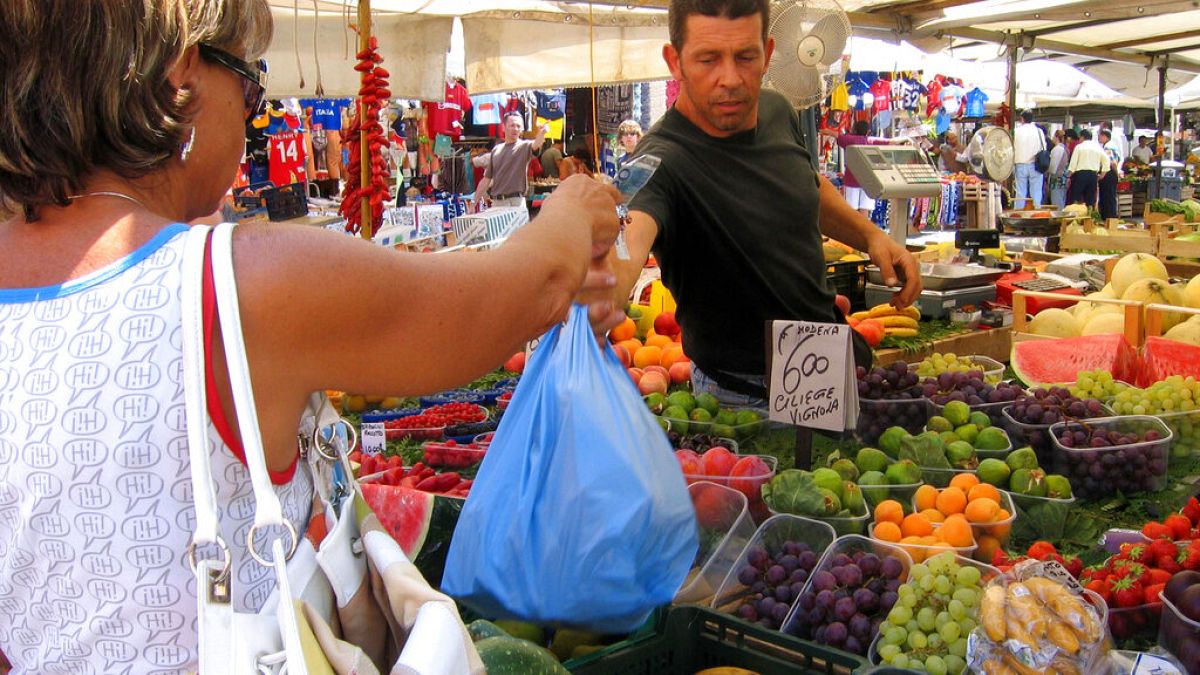 in questa immagine d'archivio, una donna paga per la spesa in un chiosco di frutta e verdura in un mercato di Roma, venerdì 30 luglio 2004