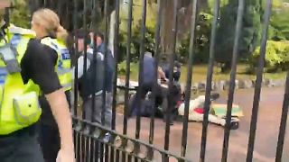 Hiter dem Tor liegt der Demonstrant am Boden und wird augenscheinlich verprügelt