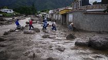 Personas vadean una carretera llena de barro tras el desbordamiento de un río provocado por las fuertes lluvias en El Castaño, Venezuela